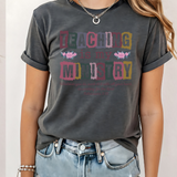 A 3x3 grid showing nine different colorful graphic t-shirts worn by a model. The shirts feature various teacher-themed designs including an apple with the word 'teach', a blue daisy pattern, a rainbow smiley face saying 'BELIEVE SUCCESSION MAKES A DIFFERENCE', a pink heart and book design, a pink and blue 'TEACH A MIDNIGHT' graphic, a rainbow lightning bolt, a patriotic 'TEACHER' design, the word 'teach' in pink script, and a gold glitter-style 'TEACH' graphic.