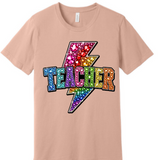 A 3x3 grid showing nine peach-colored short-sleeve t-shirts, each with a different colorful teacher-themed graphic design such as an apple, lightning bolt, and text slogans.