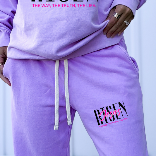 Person wearing a purple 'Risen Jesus' tracksuit against a light background